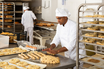 male baker in white uniform rolling out dough in kitchen