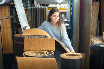 Wall Mural - Smiling woman choosing flooring samples and carpets in a building hypermarket