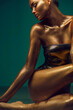 Model girl with bright golden sparkles on her body posing, full length portrait of beautiful sexy woman with glowing body skin. Swimsuit. Art design make up. Glitter gold sequins on skin body art