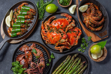 Wall Mural - Set of Seafood Dishes. Crabs, octopus, squids and tiger shrimps on cast iron pans and plates on a black background. Top view.