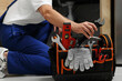 © New Africa - Professional plumber taking adjustable wrench from tool bag indoors, closeup