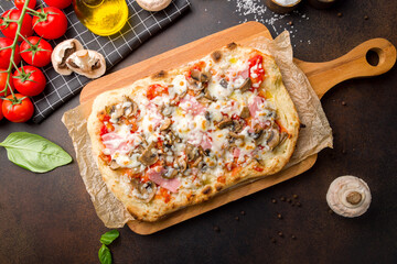 Wall Mural - Roman pizza with ham and mushrooms on Roman dough, pinsa on dark brown table top view