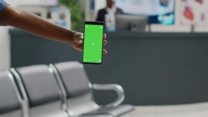 Female professional nurse holding mobile phone with greenscreen, using chroma key display in hospital reception. Person looking at isolated copyspace with mockup background, waiting room.