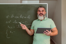 Mature Teacher With Tablet PC Teaching Mathematics On Chalkboard