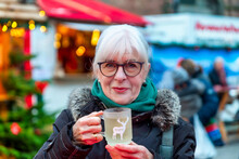 Smiling senior woman with cup of mulled wine at Christmas market