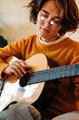 © Drobot Dean - Brunette young woman playing guitar while sitting on armchair