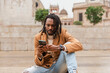 © Renata Hamuda - a stylish modern man with dreadlocks sitting in the city outdoors using smartphone