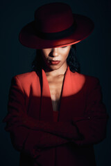 Canvas Print - Fashion, red suit with spotlight for woman in dark, mystery and 90s retro on a black studio background. Designer, power and model with vintage clothes, arms crossed and makeup for empowerment