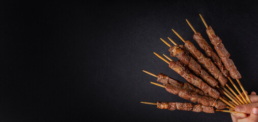 Lamb skewers also called kebabs, or arrosticini or chuan, are small pieces of meat roasted on wooden skewers over charcoal.  Black background, banner size, copy space.