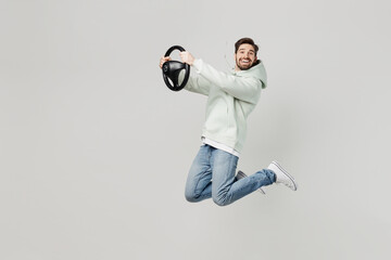Full body young side view happy satisfied man wear mint hoody look camera hold steering wheel driving car jump high isolated on plain solid white background studio portrait. People lifestyle concept.