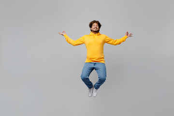 Wall Mural - Full body young Indian man 20s he wearing casual yellow hoody jump high hold spreading hands in yoga om aum gesture relax meditate try to calm down isolated on plain grey background studio portrait
