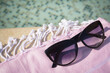 Stylish sunglasses and blanket near outdoor pool on sunny day, closeup. Space for text