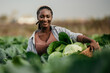 © La Famiglia - Portrait of a dedicated black woman holding a crate full of fresh cabbage in her hands on the farm outdoors.