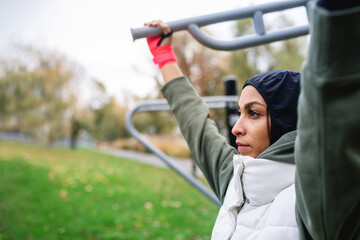 Wall Mural - Young muslim woman in sports hijab doing work out in outdoor training ground.