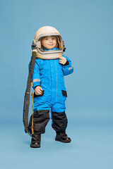 Portrait of little boy, child posing in astronaut costume over blue studio background. Space researcher