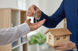 © Studio Romantic - Real estate agent hands over key to customer after signing home purchase agreement. Close up of man's hand holding small wooden model house and handing keys to another man's hand. Real estate concept.