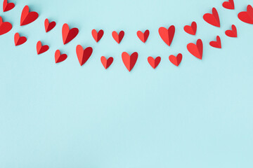 Valentine day greeting card or banner. Paper red hearts garland on blue background.