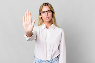 Wall Mural - caucasian blonde woman looking serious showing open palm making stop gesture