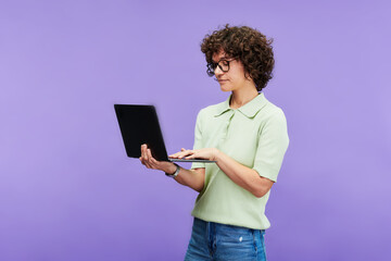 Poster - Young serious brunette woman in casualwear typing on laptop keyboard while networking on studying online against lilac background
