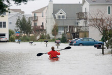 A Woman Paddles A Sea Kayak Down The Middle Of A Flooded Road.; Hampton, Virginia.