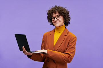 Poster - Happy young successful teacher with laptop looking at camera while standing in isolation on violet background during photo session in studio