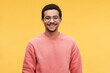 © pressmaster - Young cheerful man in eyeglasses and pink sweatshirt looking at camera while standing against vivid yellow background in isolation