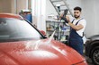 © Sofiia Shunkina - Cleaning car using high pressure water. Handsome young man worker washing modern red car hood under high pressure water in car wash service.