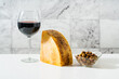 a piece of parmesan or pecorino cheese on a white table and red wine in a glass. still life