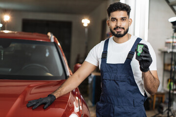 Bearded young male inspector measuring paint cover thickness of the car body at the vehicle service box, side view of hands and professional thickness meter