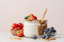 Natural Yogurt In Jar With Granola And Fresh Strawberries And Blueberries On Light Table And Beige Background. Healthy Homemade Breakfast Concept