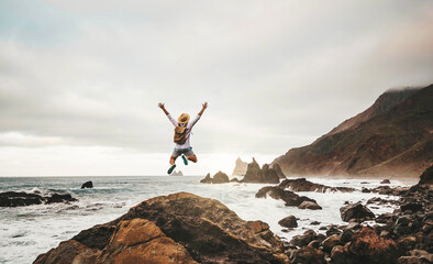 Wall Mural - Happy man with backpack jumping on nature background - Successful hiker enjoying freedom climbing rocks outdoors - Adventure, journey, freedom and sport concept