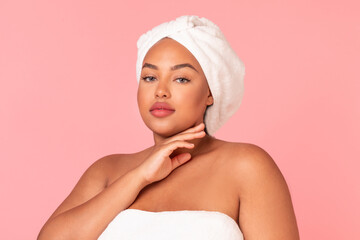 Attractive african american oversize lady with perfect skin posing wrapped in bath towel over pink studio background