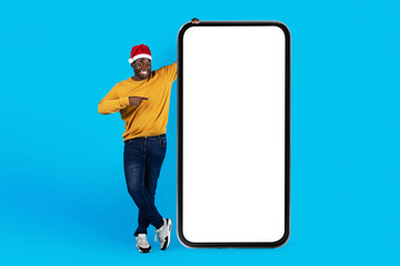 Wall Mural - Online Offer. Happy Black Man In Santa Hat Pointing At Blank Smartphone