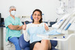 © JackF - Happy cute latin woman sitting in dental chair after teeth cure giving thumb up