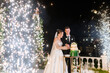 Special moment beutiful bride with groom cuts a wedding cake standing near bright sparklers. Wedding celebration party. Loving couple man and woman in puffy wedding dress. Wedding arch on a background