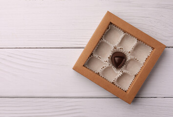 Canvas Print - Partially empty box of chocolate candies on white wooden table, top view. Space for text