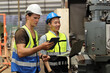 © feeling lucky - Technician engineer in protective uniform with hardhat standing and teaching apprentices or colleague worker to use computerized machine control at heavy industry manufacturing factory