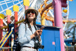 portrait of cheerful asian Taiwanese girl backpacker wearing sunglasses exploring in amusement park using travel guide on phone on ferris wheel background