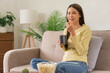 © Pichsakul - Concept of activity in home, Young woman is drinking coffee and eating popcorn while watching tv