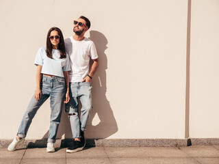 Smiling beautiful woman and her handsome boyfriend. Woman in casual summer jeans clothes. Happy cheerful family. Female having fun. Sexy couple posing in the street at sunny day. Near white wall