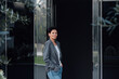 © Maria - Brunette young woman in a jacket and jeans standing at the door of a building.