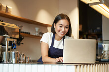 Portrait Of Smiling Asian Barista, Cafe Owner Entrepreneur, Working On Laptop, Processing Orders On Computer, Standing Behind Counter