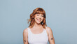 © Jacob Lund - Young, cheerful woman with ginger hair stands in a studio setting, wearing a tank top and smiling at the camera.