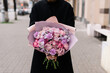 Very nice young woman holding big and beautiful bouquet of fresh carnations, roses, chrysanthemum, matthiolas, flowers in purple and pink colors, cropped photo, bouquet close up