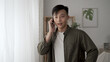 © PRPicturesProduction - cheerful asian man receiving notification call on his smartphone while standing by the window at home.