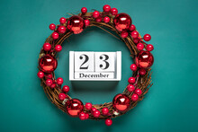Christmas Wreath Decorated With Red Berries, Wooden Calendar Date 23 December Isolated On Green Background Concept Of Christmas Preparation, Atmosphere Wishes Card Hand Made Christmas Wreath Flat Lay