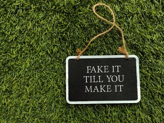 Chalkboard on grass background with text written Fake It Til You Make It , act the way into new habits until that behavior will become more of a habit and begin to come more easily