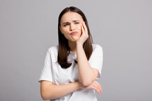 Crying Tired Sad Woman Suffers From Painful Toothache Dental Illness Pointing On Teeth Standing On Grey Background In Studio Isolated Wearing Basic White T-shirt.