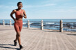 Black woman running at beach promenade for fitness, energy and strong summer body. Runner, healthy female and sports wellness at ocean for marathon goals, cardio exercise and workout in sunshine