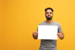 © Martin Villadsen - Handsome young man over yellow background holding blank paper sheet contract with a happy face. Confident and smiling Jamaican guy.